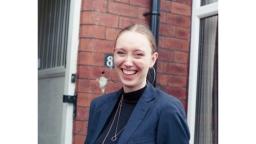 A woman smiling and wearing large hoop earrings, a black top, and navy blazer.